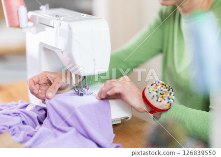 Closeup of woman hands and sewing machine - process of making clothes Closeup of woman hands and sewing machine - process of making clothes 126839550
