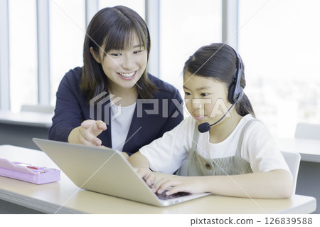 Elementary school girl and teacher studying on a laptop at a cram school. Photo courtesy of Tokyo Electronics College of Denpa Gakuen, a private school corporation. Elementary school girl and teacher studying on a laptop at a cram school. Photo courtesy of Tokyo Electronics College of Denpa Gakuen, a private school corporation. 126839588