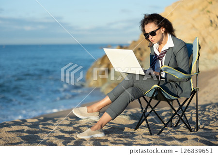 Businesswoman in office clothes working on laptop on seashore Businesswoman in office clothes working on laptop on seashore 126839651