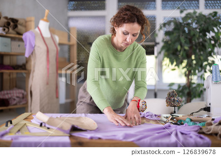 Female tailor pinning paper pattern to fabric in workshop Female tailor pinning paper pattern to fabric in workshop 126839678