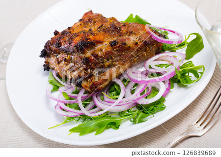 Tasty pork ribs baked under sauce, served with arugula and onion salad Tasty pork ribs baked under sauce, served with arugula and onion salad 126839689