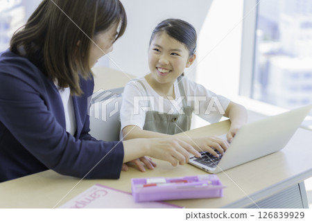 Elementary school girl and teacher studying on a laptop at a cram school. Photo courtesy of Tokyo Electronics College of Denpa Gakuen, a private school corporation. 126839929