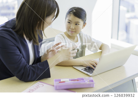 Elementary school girl and teacher studying on a laptop at a cram school. Photo courtesy of Tokyo Electronics College of Denpa Gakuen, a private school corporation. 126839932
