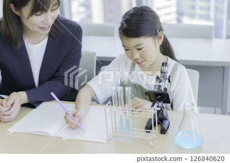 Elementary school girl and teacher looking through a microscope. Photo courtesy of Tokyo Electronics College, Denpa Gakuen School Corporation. 126840620