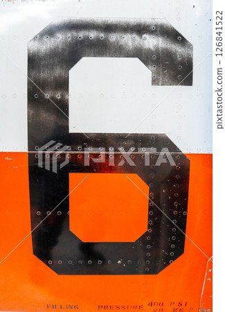 Large black number -6- on an old aircraft fuselage with rivets 126841522