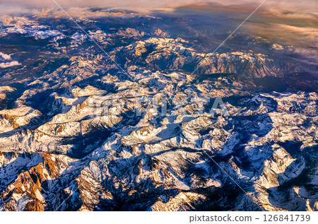 Aerial view of the snow-covered Sierra Nevada mountains in California during sunset, revealing dramatic peaks and rugged terrain with golden light highlighting the landscape 126841739
