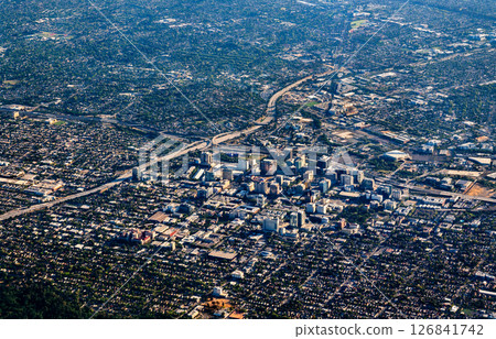 Expansive aerial view of San Jose, California, featuring a dense urban downtown core surrounded by sprawling residential neighborhoods, visible highways, and scattered green spaces under clear 126841742