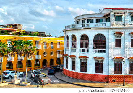 Vibrant street scene in Cartagena, Colombia featuring historic colonial buildings with arched windows, colorful facades, palm trees, and parked cars under a partly cloudy sky. Vibrant street scene in Cartagena, Colombia featuring historic colonial buildings with arched windows, colorful facades, palm trees, and parked cars under a partly cloudy sky. 126842491