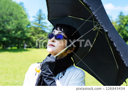 A middle-aged woman protecting herself from UV rays with a parasol, scarf, gloves and sunglasses A middle-aged woman protecting herself from UV rays with a parasol, scarf, gloves and sunglasses 126843434