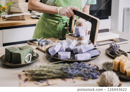 Handmade lavender soaps arranged on a kitchen table with a soap cutter and dried flowers. Themes include natural skincare products, aromatherapy, zero-waste beauty 126843622