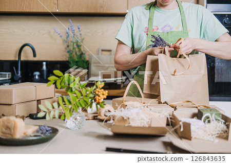 Person wraps natural soaps in kraft packaging for a small business in a home kitchen. Handmade product packaging, creative process, DIY business visuals, home-based business 126843635