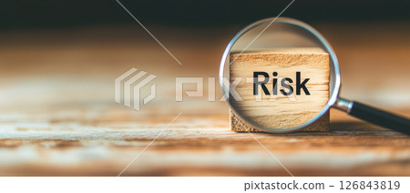 Magnifying glass highlighting wooden block with word Risk, symbolizing analysis and evaluation of potential challenges 126843819