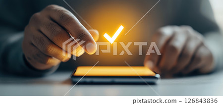 Professional hand touching smartphone screen with glowing check mark, symbolizing approval and technology 126843836