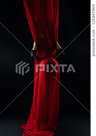 Model posing elegantly behind flowing red fabric in a dramatic setting Model posing elegantly behind flowing red fabric in a dramatic setting 126843969