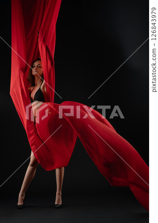 Model posing elegantly with flowing red fabric in a dramatic casting session 126843979