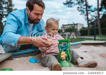 Father and little toddler son playing in the sandbox on playground. Father and little toddler son playing in the sandbox on playground. 126844017