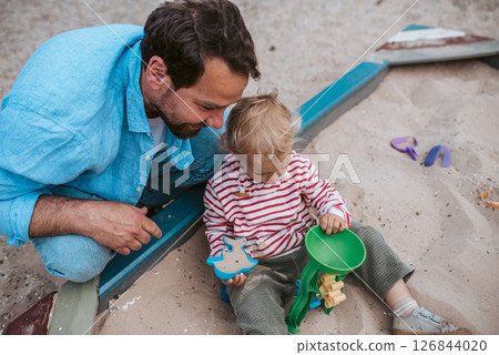 Father and little toddler son playing in the sandbox on playground. Father and little toddler son playing in the sandbox on playground. 126844020