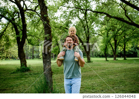 Father carrying his smiling son on shoulders during walk in park 126844048