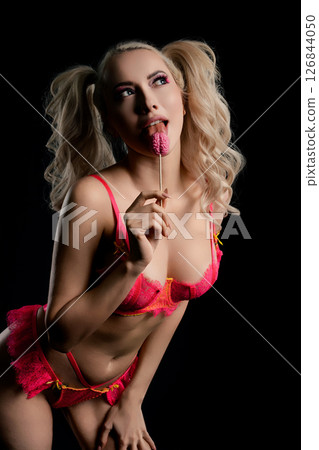 Woman poses playfully in vibrant lingerie while holding a candy treat 126844050