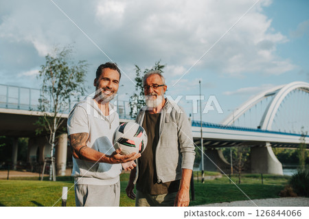 Sporty father and adult son playing football in park, throwing ball. 126844066