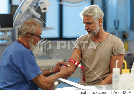 Older doctor drawing blood from patient's arm. 126844209