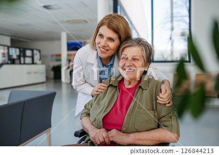 Elderly patient in wheelchair and female physician smiling at clinic. Elderly patient in wheelchair and female physician smiling at clinic. 126844213