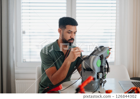 Engineer assembling and coding a robotic arm at home as part of a robotics project. 126844302
