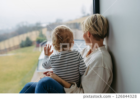 Boy and mother looking out of window. Boy and mother looking out of window. 126844328