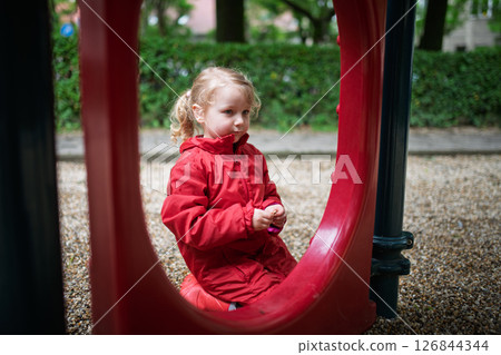 Child in red coat resting at play area. 126844344
