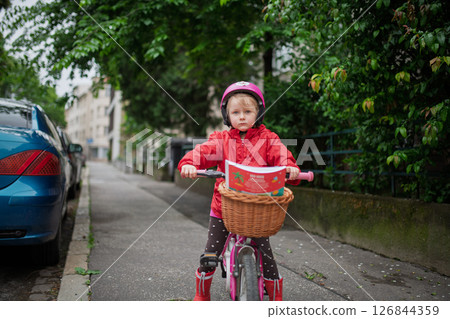 Little girl riding pink bike with basket, wearing helmet. 126844359