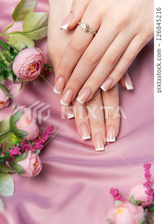 Woman showing french manicure on pink satin background with flowers 126845216