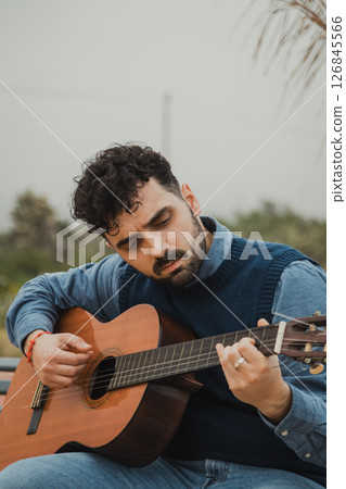 Man Plays Guitar Sitting on a Bench Outdoors 126845566