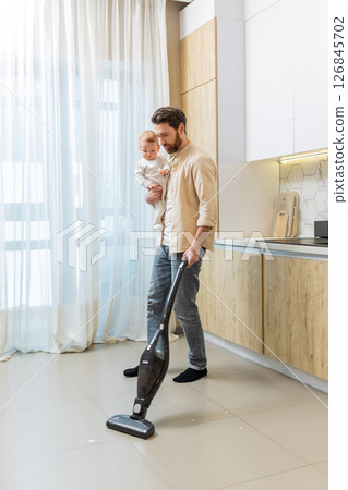 Young single dad cleaning the house while holding his son in his hands 126845702