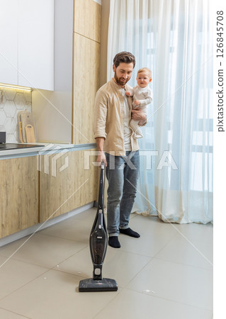 Young single dad cleaning the house while holding his son in his hands Young single dad cleaning the house while holding his son in his hands 126845708