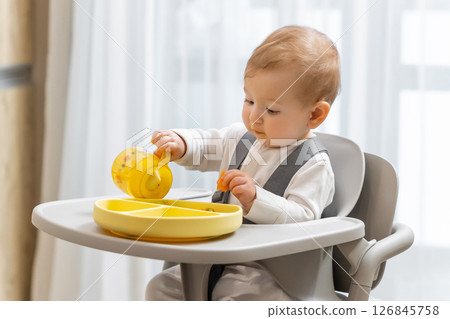 Cute baby boy sitting on his chair and eating from his yellow plate 126845758