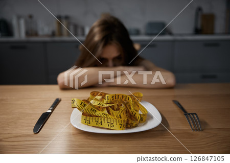 Depressed anorexic woman looking at plate with measuring tape served for dinner 126847105