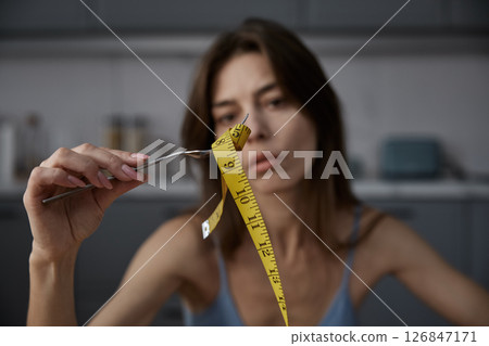 Sad skinny thin woman eating measuring tape demonstratively at home kitchen 126847171