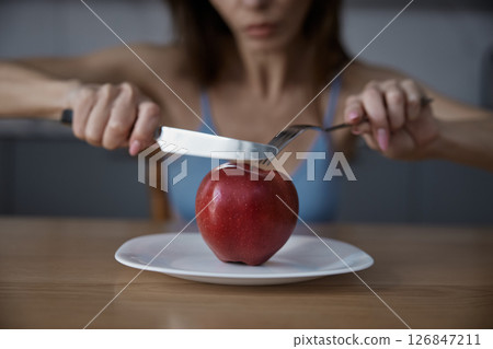 Skinny anorexic woman eating apple sitting at dining table in home kitchen 126847211