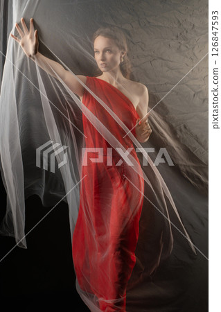 Woman in a flowing red dress expresses emotion while posing in a studio with sheer fabric on display 126847593