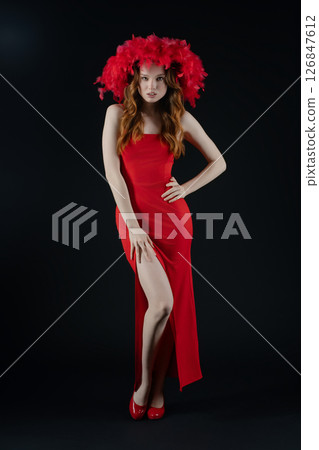 Woman in a striking red dress poses confidently in the studio, showcasing emotion and vibrancy with a feathered headpiece and playful expression 126847612
