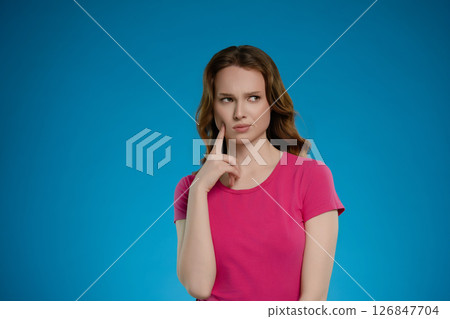 Woman posing thoughtfully in a studio setting with an emotional expression against a bright blue background Woman posing thoughtfully in a studio setting with an emotional expression against a bright blue background 126847704