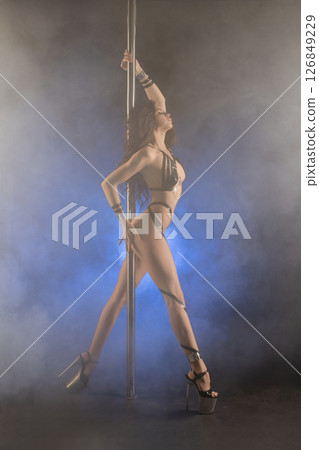 Brunette pole dancer showcases beauty with tape bodyart in dramatic lighting 126849229