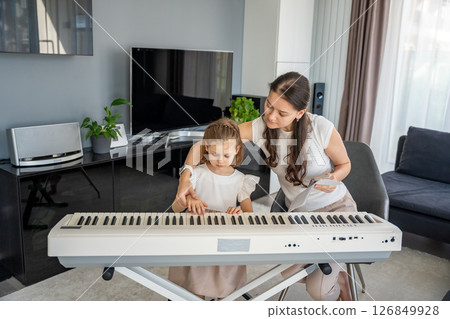 Individual piano lesson for a young child at home in the living room. Concept of early childhood development through personalized music education. Individual piano lesson for a young child at home in the living room. Concept of early childhood development through personalized music education. 126849928
