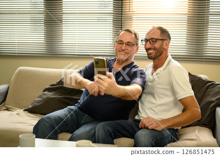 Elderly dad and grown up son relax on sofa and take a cheerful selfie together. Father day concept Elderly dad and grown up son relax on sofa and take a cheerful selfie together. Father day concept 126851475