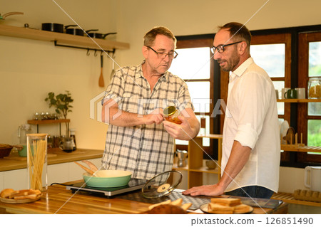 Happy senior man and grown son preparing pasta dish in a bright kitchen. Father day concept 126851490