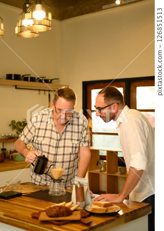 Senior man and grown son preparing hand-brewed coffee at a wooden kitchen counter. Father day concept Senior man and grown son preparing hand-brewed coffee at a wooden kitchen counter. Father day concept 126851513
