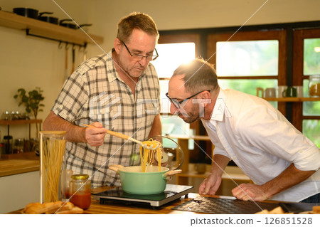 Happy senior man and grown son preparing pasta dish in a bright kitchen. Father day concept Happy senior man and grown son preparing pasta dish in a bright kitchen. Father day concept 126851528