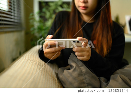 Young woman in black sweatshirt scrolling on her phone, relaxing in a softly lit room Young woman in black sweatshirt scrolling on her phone, relaxing in a softly lit room 126851544