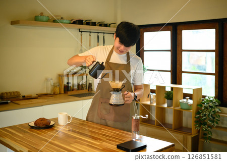 Smiling man prepares a fresh cup of drip coffee at his kitchen counter 126851581