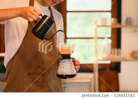 Man wearing an apron preparing fresh pour over coffee in a cozy kitchen 126851582